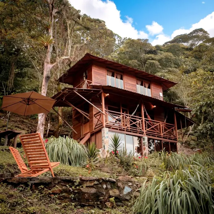 La cabaña de madera de dos niveles vista desde el jardín, entre el bosque.