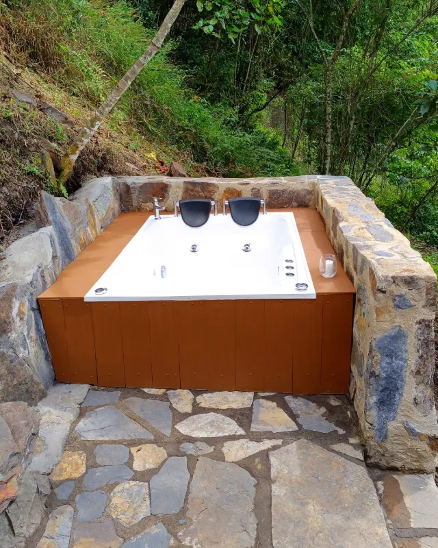 El jacuzzi de piedra de la cabaña, de día, rodeado de bosque.