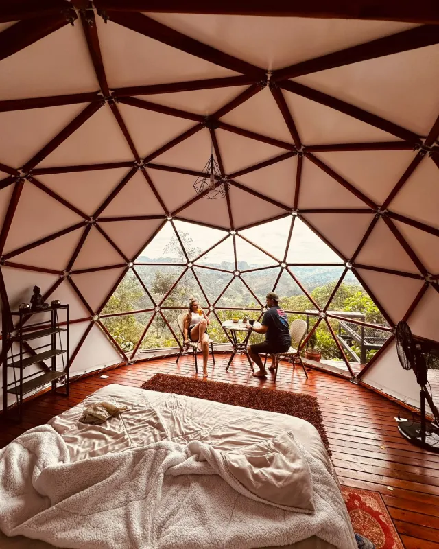 Interior del domo con la cama y la ventana triangular abierta al paisaje.