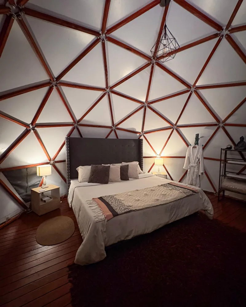 Interior del domo: la cama king bajo la estructura geodésica de madera.